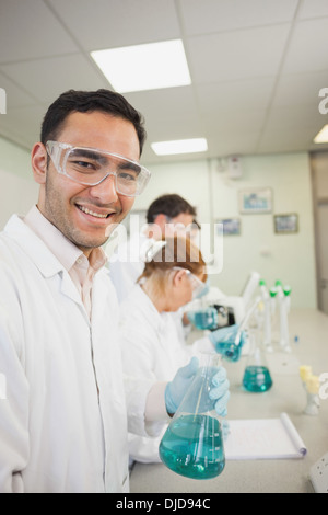 Giovane maschio scienziato tenendo un matraccio Erlenmeyer in piedi in un laboratorio Foto Stock