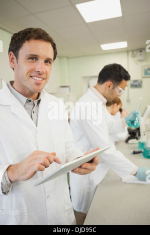 Bel giovane scienziato utilizzando il suo tablet permanente, mentre in laboratorio Foto Stock