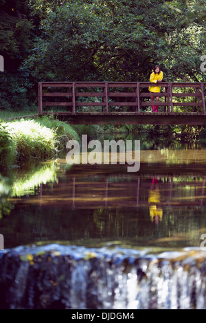 Donna sulla passerella sul lago e nel mezzo di fogliame Foto Stock