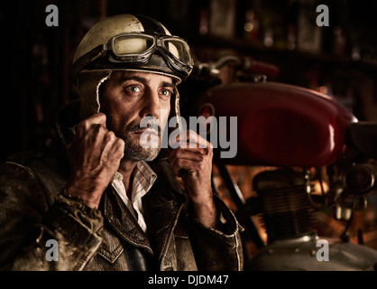 L'uomo con la vecchia giacca di pelle a mettere su un vecchio casco del motociclo Foto Stock