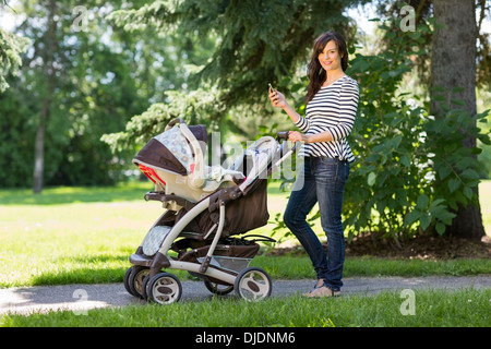 Madre con un telefono cellulare e il trasporto a piedi in posizione di parcheggio Foto Stock