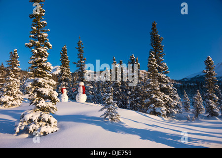 Due pupazzi di neve che indossa foulard rosso e nero in alto cappelli e in piedi di fronte a un abete Snowcovered Forest Chugach Mountains Foto Stock