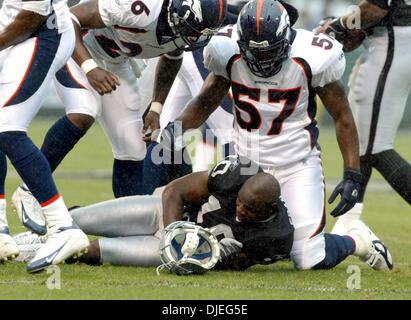 Oct 17, 2004; Oakland, CA, Stati Uniti d'America; NFL Football: con la pioggia è caduta#10 per i raider Carlos Francesco ottiene il suo casco colpisci da #57 per i Broncos Jashon Sykes sul affrontare con #26 per cavalli selvaggii Tatum Bell cerca su nel terzo trimestre. Foto scattata durante i raider vs Broncos gioco presso la Network Associates Coliseum. Foto Stock