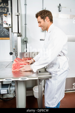 Sorridente macellaio il taglio di carne a fette sulla segatrice a nastro Foto Stock