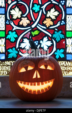 Tutti Hallows Eve. Un Halloween Jack O' Lantern intagliati da una zucca, incandescente a lume di candela, di fronte a una finestra di vetro colorato. Inghilterra, Regno Unito. Foto Stock