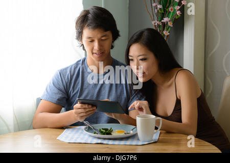 Una giovane coppia asiatica siting fianco a fianco avendo divertimento giochi su un ipad, compressa al mattino la prima colazione. Foto Stock