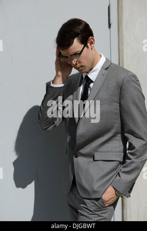 Un giovane uomo di affari che indossa gli occhiali vintage guardando in giù a piedi con una mano in tasca, pensando, decidere. Foto Stock
