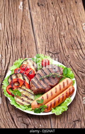 Bistecca alla griglia,salsicce e verdure sopra le foglie di lattuga su un tavolo di legno. Foto Stock