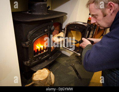 Uomo di mettere un log su una stufa a legna Foto Stock