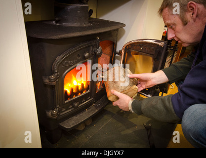 Uomo di mettere un log su una stufa a legna Foto Stock