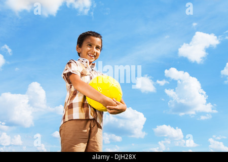 Carino piccolo ragazzo in piedi con il calcio palla in mano sopra il cielo blu Foto Stock