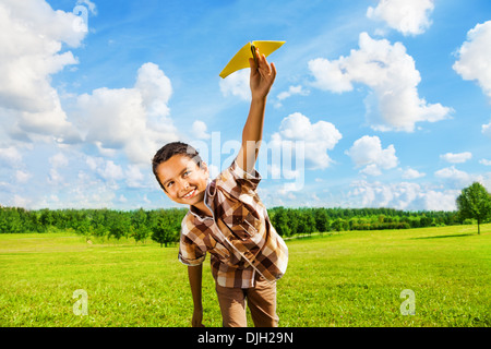 Felice ragazzo inclinazione e gettando giallo aeroplano di carta sulla luminosa giornata di sole nel campo Foto Stock