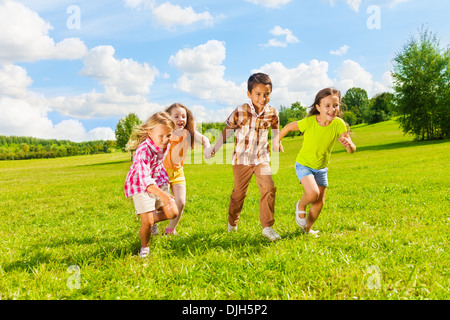 Un gruppo di piccoli 6 e 7 anni di età i bambini e i ragazzi e le ragazze in esecuzione tenendo le mani insieme nel parco Foto Stock