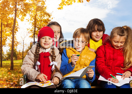 Il gruppo di cinque bambini intorno 10 anni disegno delle immagini al di fuori seduta in autunno il giorno Foto Stock