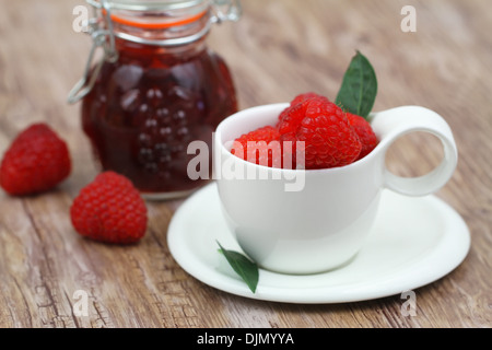 Tazza bianca con lamponi freschi e vintage jar con confettura di lamponi Foto Stock