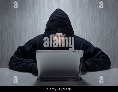 Un maschio con cappuccio che rappresenta un cyber criminali, utilizzando un computer tablet. Foto Stock