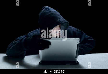 Un anonimo maschio incappucciati che rappresentano un cyber criminali, utilizzando un computer tablet. Foto Stock