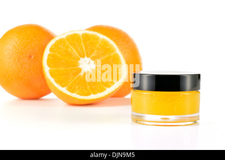 Arancio naturale di zucchero macchia a labbro su sfondo bianco. Cosmetici arancio in un vaso di vetro con le arance in uno sfondo. Foto Stock