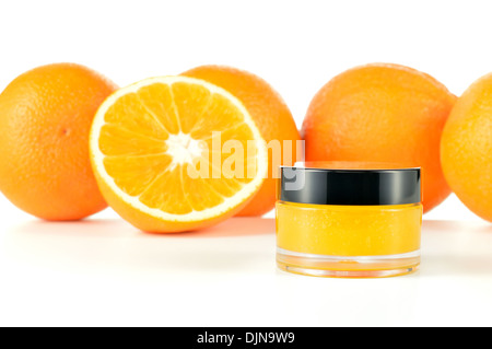 Arancio naturale di zucchero macchia a labbro su sfondo bianco. Cosmetici arancio in un vaso di vetro con le arance in uno sfondo. Foto Stock