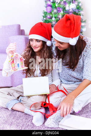 Bella madre dando presente a sua figlia carino, felice espressione facciale, bellissimo albero di Natale decorato, amorevole famiglia Foto Stock