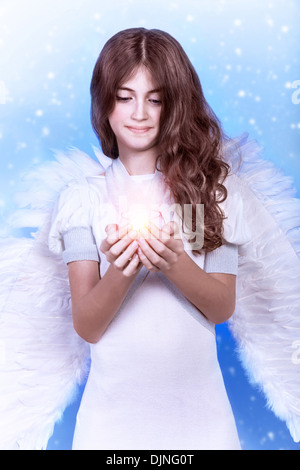 Ritratto di bella angelo, dolce ragazza teen indossando abito bianco e grandi e soffici ali blu su sfondo innevato, tenendo candela Foto Stock