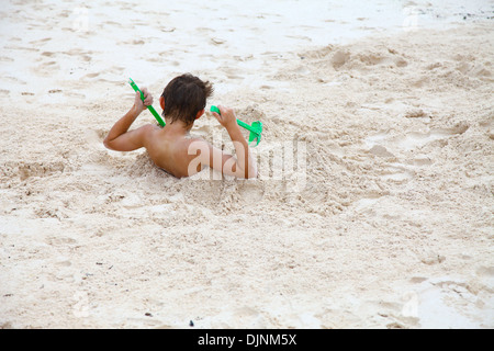 Un giovane ragazzo di seppellimento di se stesso nella sabbia bianca sulla spiaggia in Riviera Maya Cancun Penisola dello Yucatan Messico America del Nord Foto Stock