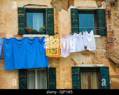 Vivacemente colorato biancheria appesa sulla linea di lavaggio tra finestre con persiane, Venezia, Italia Foto Stock