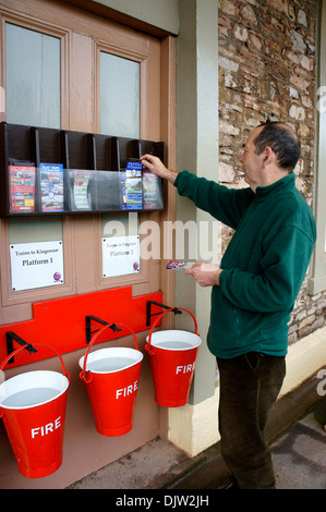 L'uomo prendendo il treno calendario & Opuscoli a Churston stazione ferroviaria, Devon, Inghilterra. Foto Stock