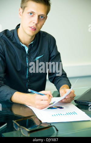 Giovane imprenditore seduta a tavola e lavorare con i grafici Foto Stock