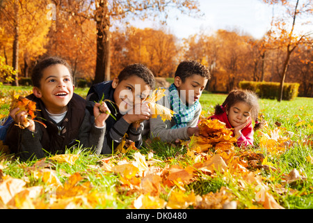 Il gruppo di quattro ragazzi di colore nero e una ragazza, felice fratelli e sorelle 3-10 anni posa in erba insieme nel parco in autunno gli abiti sotto il parco di acero con foglie di colore arancione Foto Stock