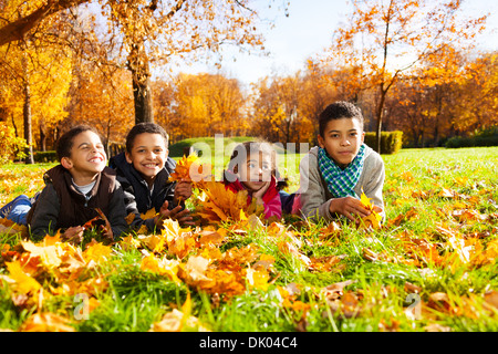 Il gruppo di quattro ragazzi di colore nero e una ragazza, felice fratelli e sorelle 3-10 anni posa in erba insieme nel parco in autunno Vesti holding foglie di acero mazzi Foto Stock