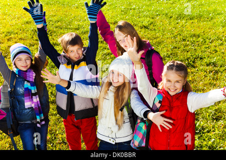 Chiudere il ritratto di un gruppo di felice teen età i bambini della scuola in piedi sul prato con sorriso sui volti mani di sollevamento, vista dall'alto autunno indossare vestiti caldi Foto Stock