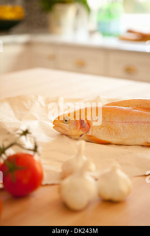 Close up di pesce intero, l'aglio ed il pomodoro di cottura Ingredienti sul banco di cucina Foto Stock