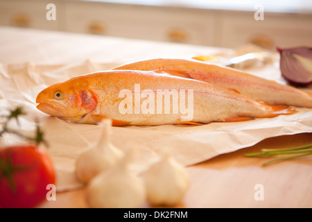 Close up di pesce intero, l'aglio ed il pomodoro ingredienti sul banco di cucina Foto Stock