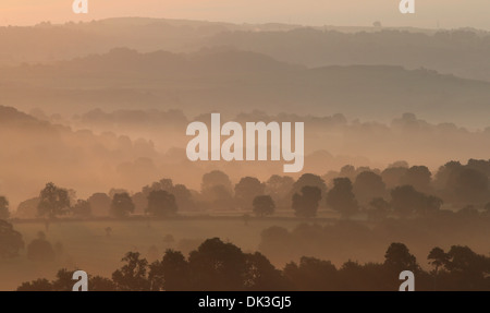 Alba rompe su tarda estate nebbia di mattina visto da di Thorpe pascolo guardando verso Tissington nel Derbyshire Peak District. Foto Stock