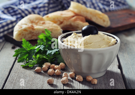 Ciotola di freschi hummus con olive e le fette di pane su sfondo di legno Foto Stock