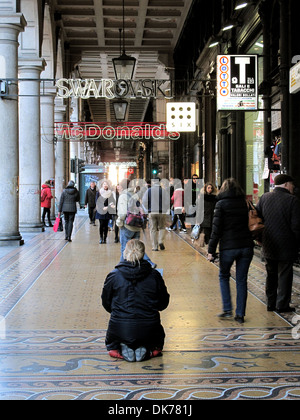 Una donna senzatetto inginocchiati su un pavimento in mosaico in un porticato lungo Via XX Settembre a Genova. Foto Stock