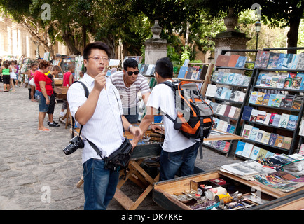I turisti cinesi a Cuba guardando i libri nel mercato, Plaza de Armas, Havana Cuba, dei Caraibi Foto Stock