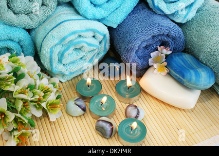 Pila di asciugamani, saponi, candele, pietre, fiori su sfondo mat. Foto Stock