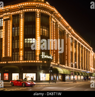 I grandi magazzini Harrods. Facciata illuminata di notte. La Ferrari passa nella parte anteriore dell'edificio Foto Stock