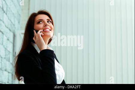 Giovane imprenditrice felice di parlare al telefono e guardando lontano a copyspace in office Foto Stock