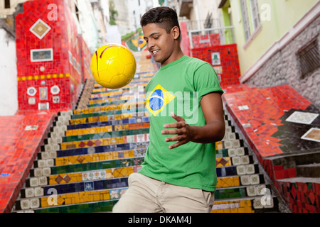 Giovane uomo che indossa il Brasile top facendo keepy uppys davanti al Escadaria Selaron passi in Rio de Janeiro, Brasile Foto Stock