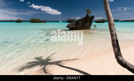L'ombra di una palma da cocco sulla spiaggia, una barca ancorata e vedute di calcare motus, piccoli isolotti eroso in laguna Fulaga Laus Isole Figi Foto Stock