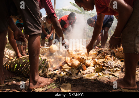 Gli uomini di apertura e la rimozione di cibo cucinato da un grande lovo (massa forno) per una festa. Namuka-i-Lau, southern Laus, Fiji. Foto Stock