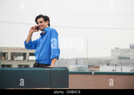 Fiducioso giovane uomo utilizzando mobile sul tetto della città Foto Stock