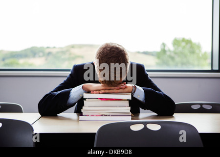 Teenage schoolboy seduto alla scrivania con la testa in giù Foto Stock