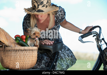 Donna matura sulla bicicletta elettrica con il cane e le verdure nel cestello Foto Stock