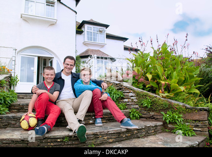 Padre e figli seduti sui passi in giardino Foto Stock