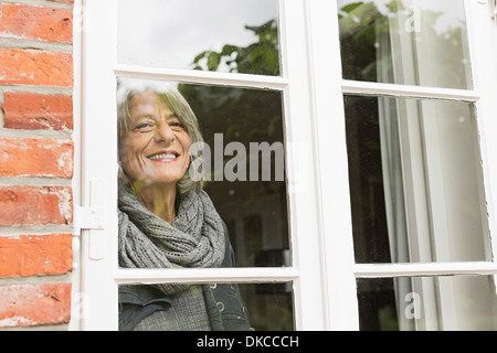 Senior donna che guarda attraverso la finestra Foto Stock