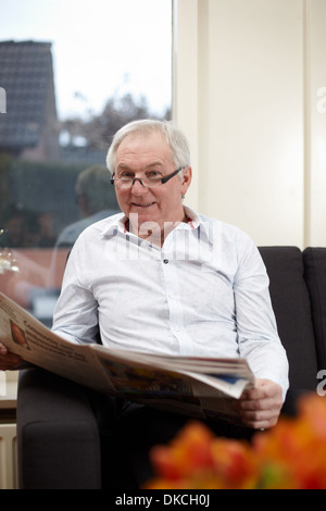 Senior man a casa leggere il giornale Foto Stock